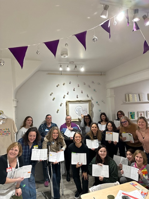 Group photo of participants holding their Bullet Journals in a creative workshop, surrounded by colorful decorations and a warm atmosphere.